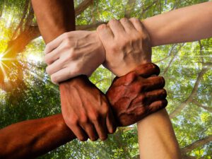 Vier Hände in vier verschiedenen Hautfarben umfassen sich an den Handgelenken, so dass ein daraus eine eine Einheit ergibt.